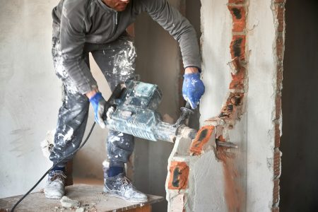 Worker drilling wall with hammer drill in building under renovation.